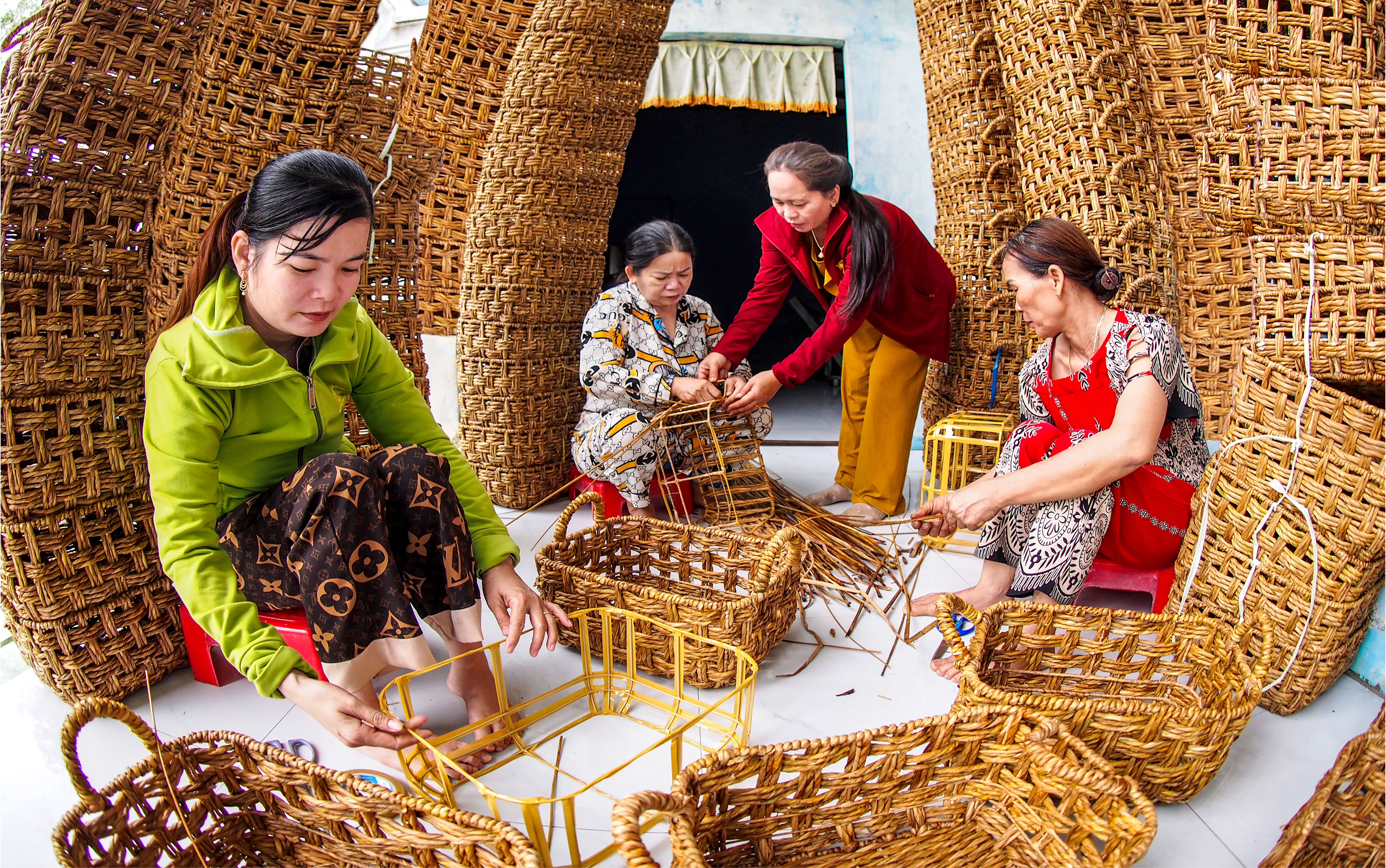 Chị Bé Tư (người đứng) hướng dẫn kỹ thuật đan sản phẩm cho chị em phụ nữ trong tổ. Sau khi lành nghề, các thành viên trong tổ tiếp tục hướng dẫn kỹ thuật cho chị em phụ nữ ở các địa phương lân cận.